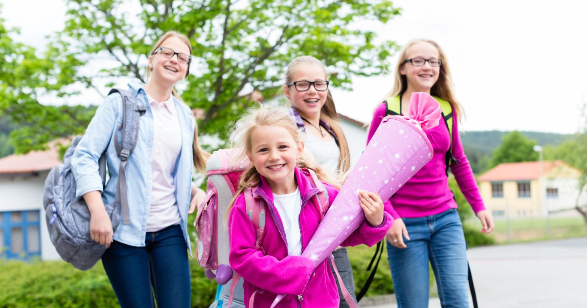 lachendes Mädchen mit rosafarbener Schultüte im Arm auf dem Weg in die Schule